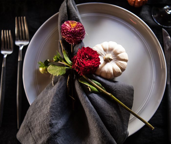 A black linen dinner napkin on a grey dinner plate, with a red flower and stem placed on top of the napkin