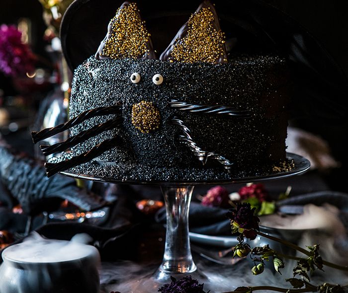 A black cat halloween themed cake. A cake with a cats face and black licorice for whiskers. Sitting on a cake stand.