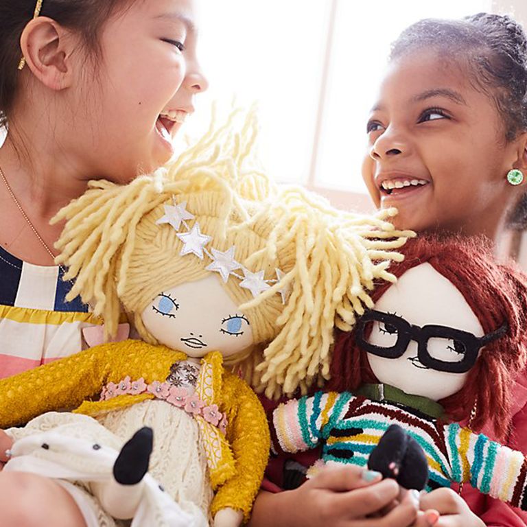Two girls holding cloth dolls and laughing