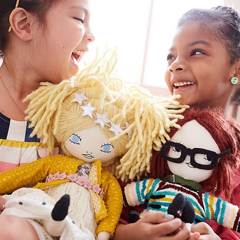 Two girls holding cloth dolls and laughing