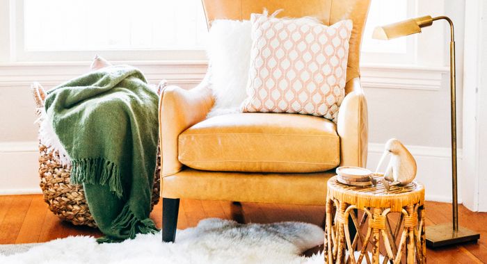  Garbo Leather Wingback Chair with two different colored pillows, next to a lamp and a basket with blankets.