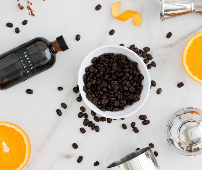 White ceramic bowl with coffee beans, next to a bottle of coffee liqueur and sliced oranges.