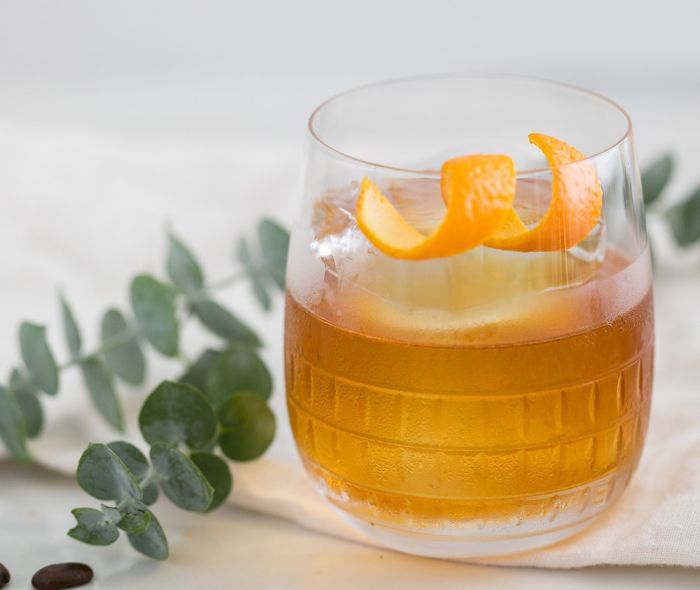 Ana Double Old-Fashioned Glass with an Old-Fashioned and an orange twist on the rim.