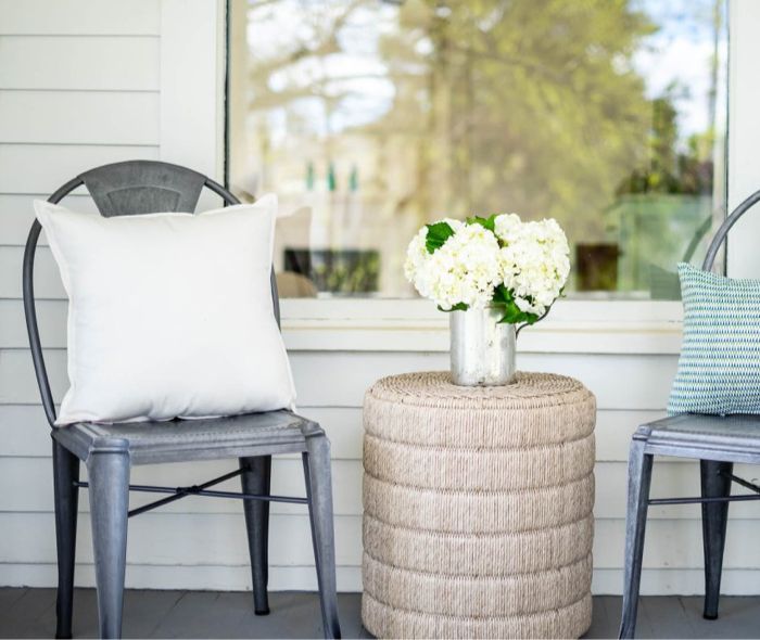 Two metal chairs with different oclores pillows and bewtween them a small textured table. 