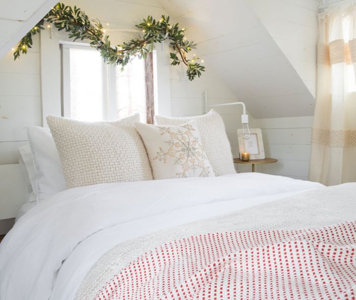 All white bedroom decorated with a green garland with yellow lights over the bed.