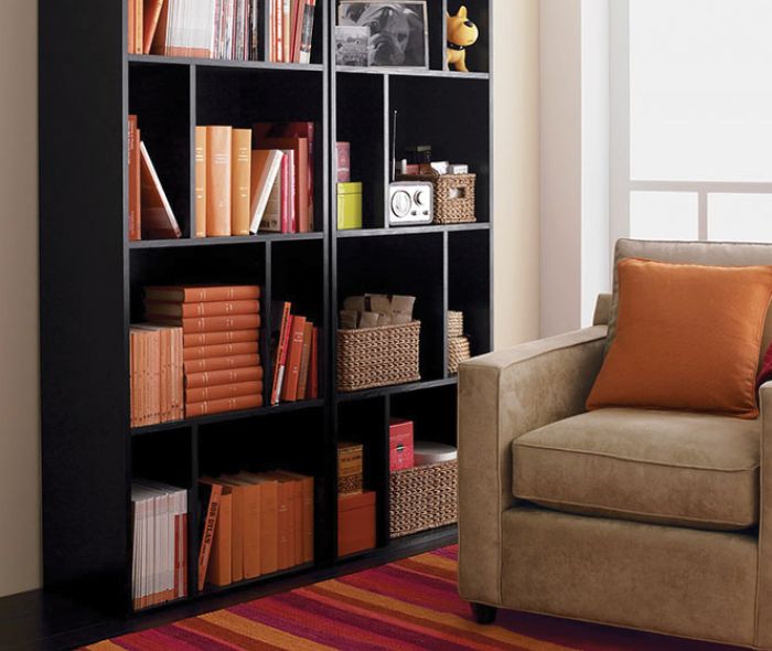 Two black bookcases next to each other with color coordinated books, baskets, and decor.