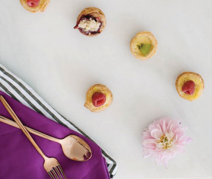 Tiny pastries with fruit next to gold flatware.