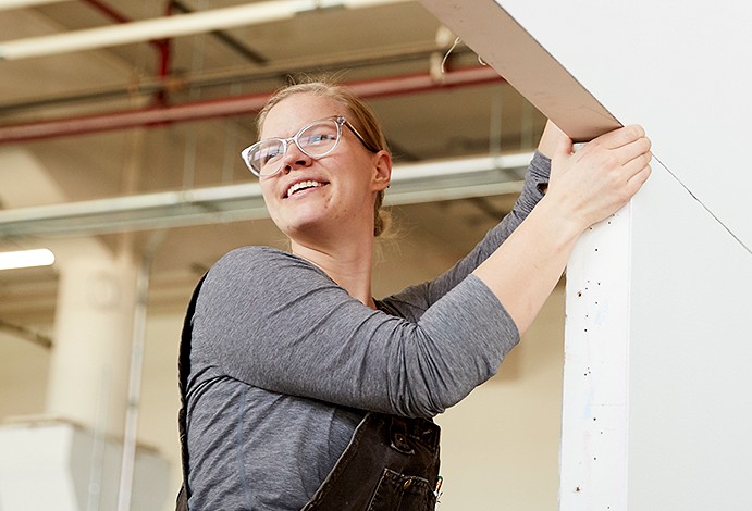 Haley smiling and working on some drywall.