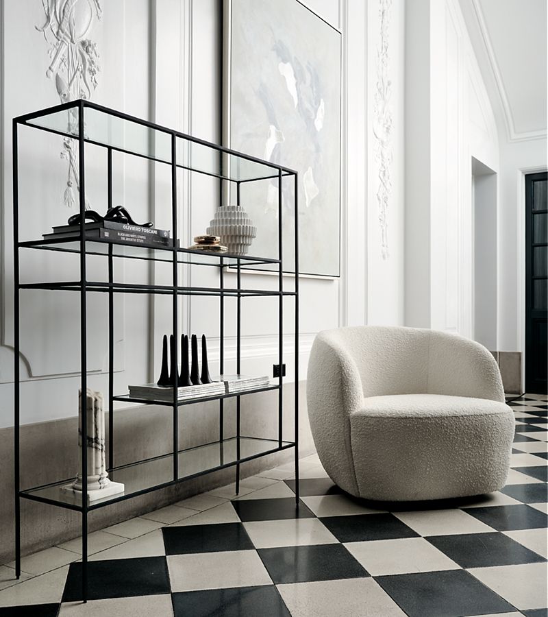 Room with plaster cast designs on the walls, checkered floor tiles and boucle swivel chair. Abstract art rests on minimalist shelf