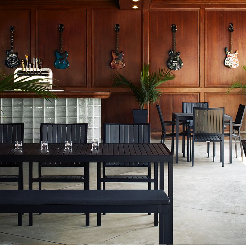 Dark bar space with with black wood furniture; walls covered with wood paneling and hanging guitar decorations