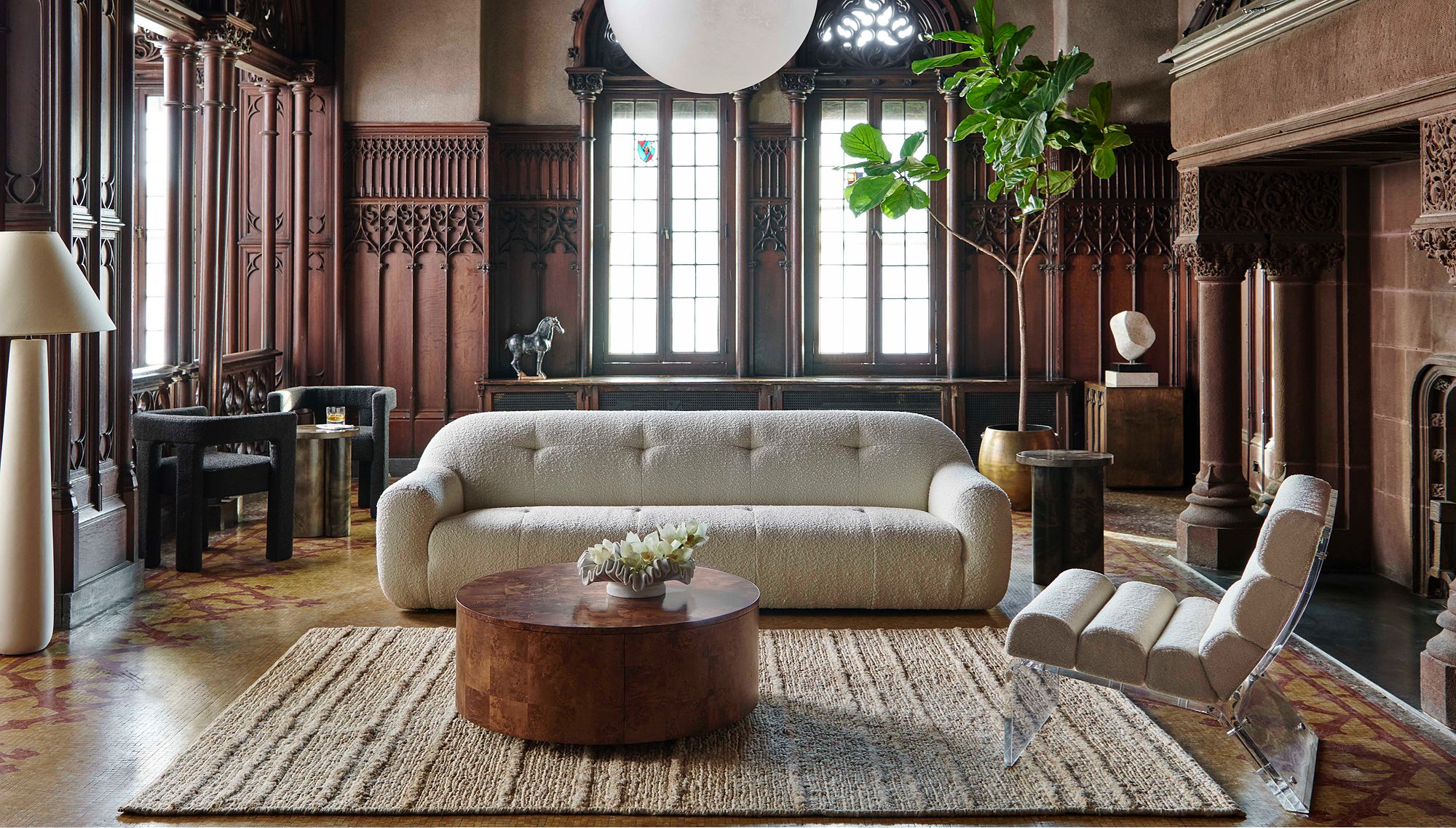 Textured sofa and round coffee table in a living room paneled with dark wood, plus gothic windows and a large fireplace