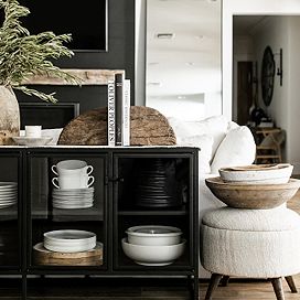 Black sideboard filled with assorted dishware and pots, with two bookends on top and a stool beside it