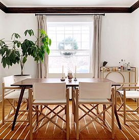 A brown table sits in the middle of a dining room, surrounded by six white and brown chairs