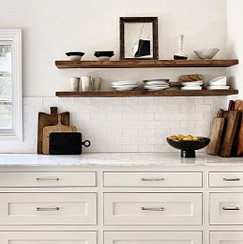 White marble kitchen counter with white drawers, and wooden shelves holding plates, bowls and cups