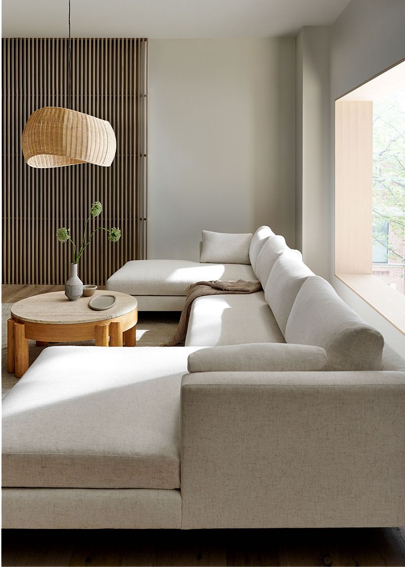 Living room with a long white sectional couch, round wood coffee table and a brown woven chandelier