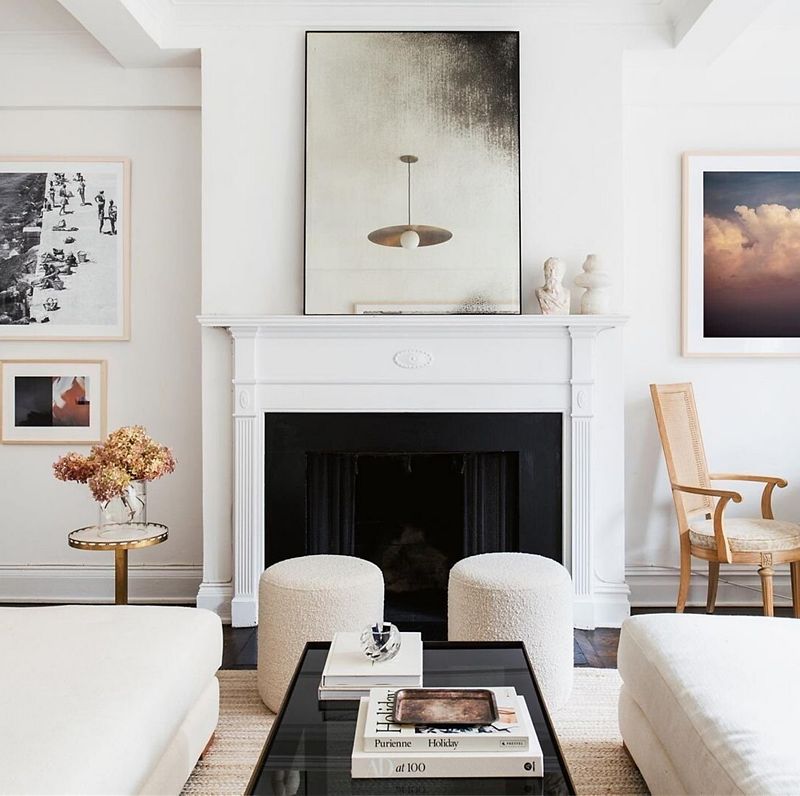 Living room with large fireplace and a piece of art on the mantel, with white upholstered seating and a black table