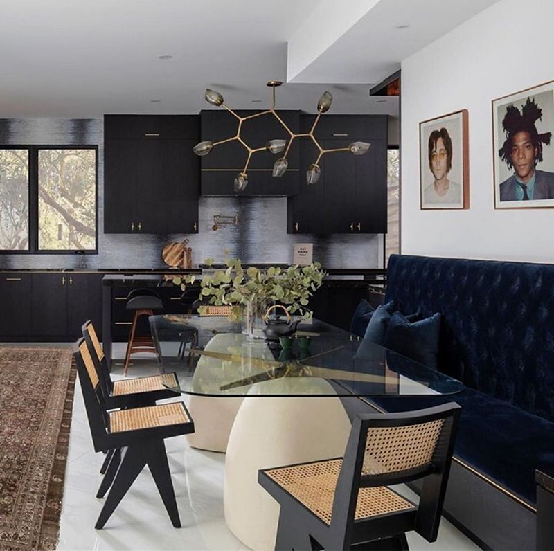 A joined dining room and kitchen space with a clear glass tabletop surrounded by a dark blue dining bench and brown and black dining chairs