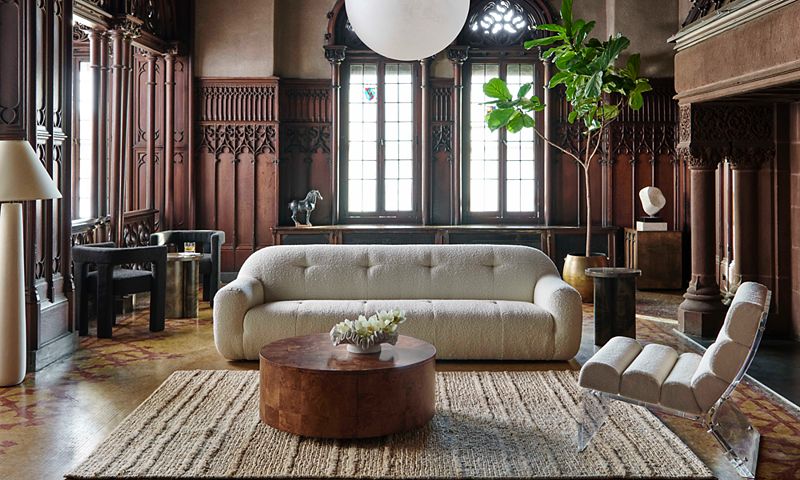 Textured sofa and round coffee table in a living room paneled with dark wood, plus gothic windows and a large fireplace