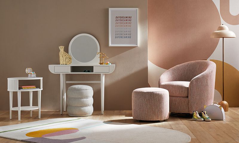 Blush-colored children's room with a light pink chair and round white mirror against the wall