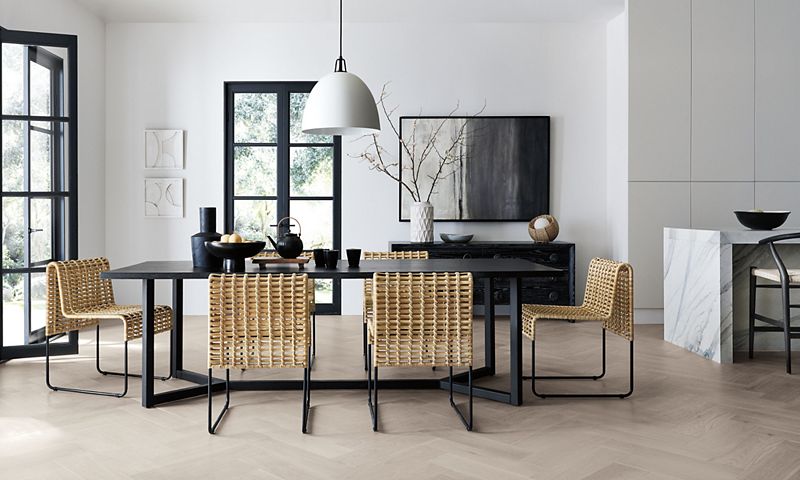 Spacious dining room with a black dining table, six brown chairs and a vase, fruit bowl and tea kettle on the table