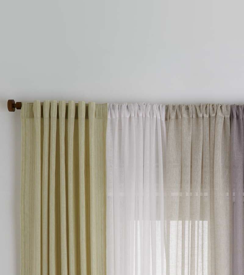 Sheer curtains in four different pastel colors hanging on a bronze curtain rod.