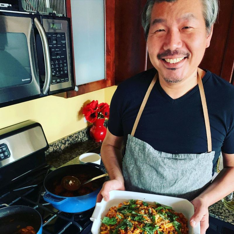 Chef Bill Kim smiling in his kitchen holding sausage pasta