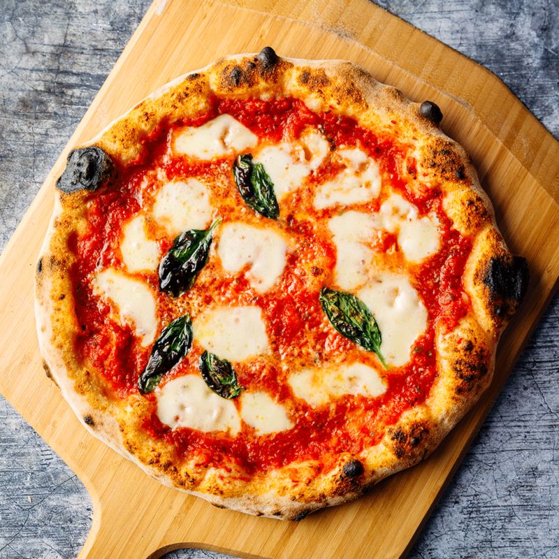 A perfectly circular margherita pizza, sprinkled 
                with asymmetrical slices of cheese and oven-crisped 
                basil leaves