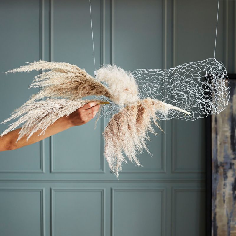 Hand placing a pampas grass stem into rolled chicken wire