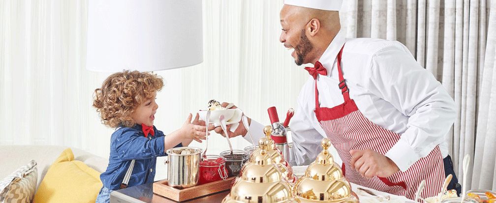 Little boy taking bowl of ice cream from a server in striped apron