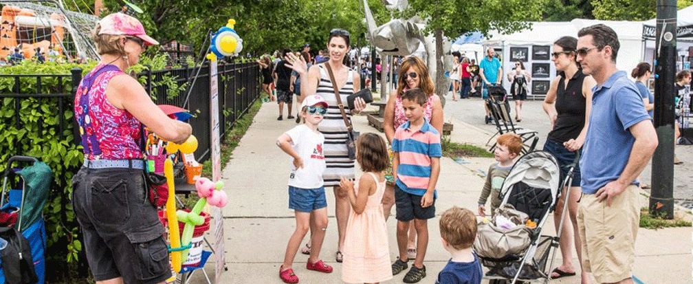 Family standing in front on a woman making balloons on the sidewalk