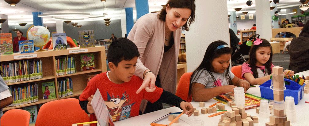 Woman pointing to something while children play with blocks at a library