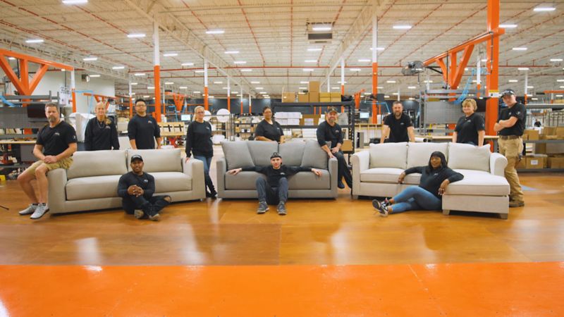 Warehouse employees posing for photo surrounding three couches