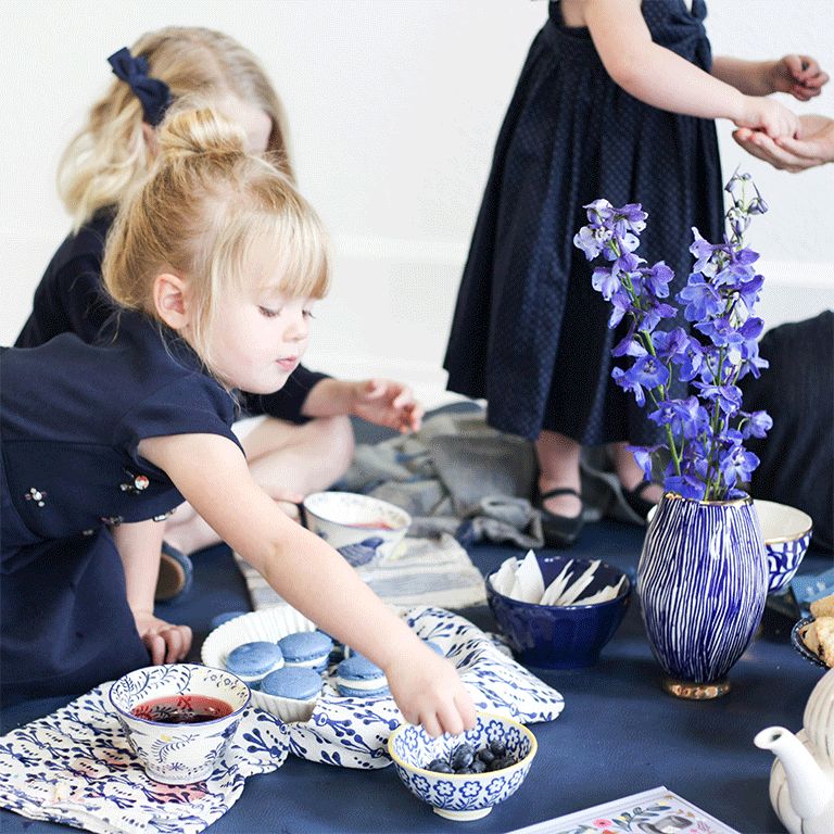 Little girl reaching for blueberries at a low table with blue willow-patterned dishes